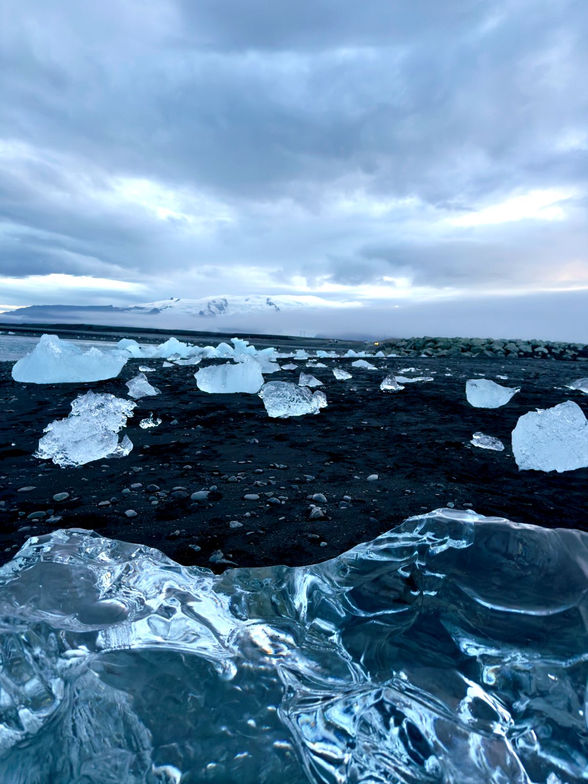 Clear chunks of glacier ice on black sand with a glacier behind
