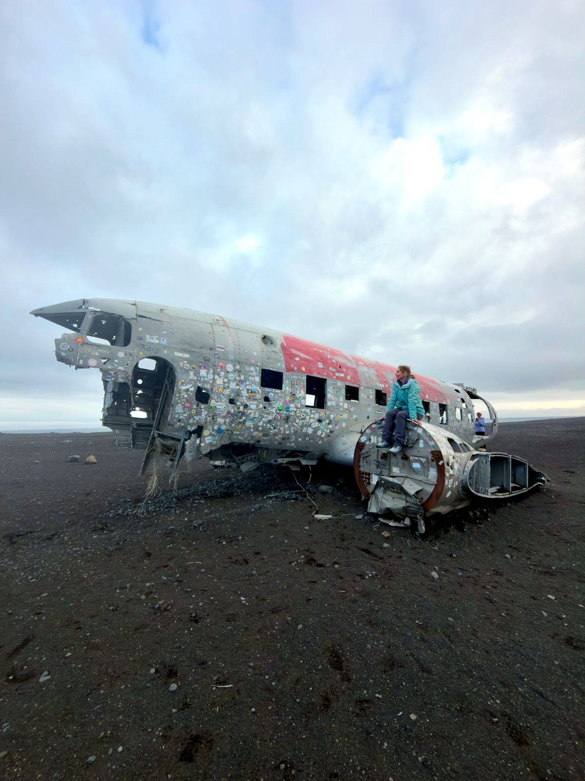 Jeanne sitting on the wreck of a DC-3 aircraft on black sand